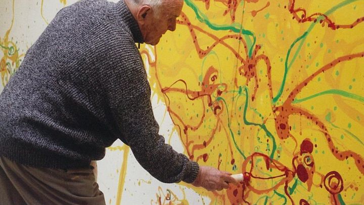 An artist painting a large yellow, red and green mural